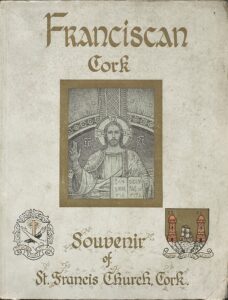 The front cover of 'Franciscan Cork: A Souvenir of St. Francis Church Cork.' The cover has detail from the apse of Christ in majesty. On the lower left is the Franciscan coat of arms and on the lower right is the coat of arms for Cork.