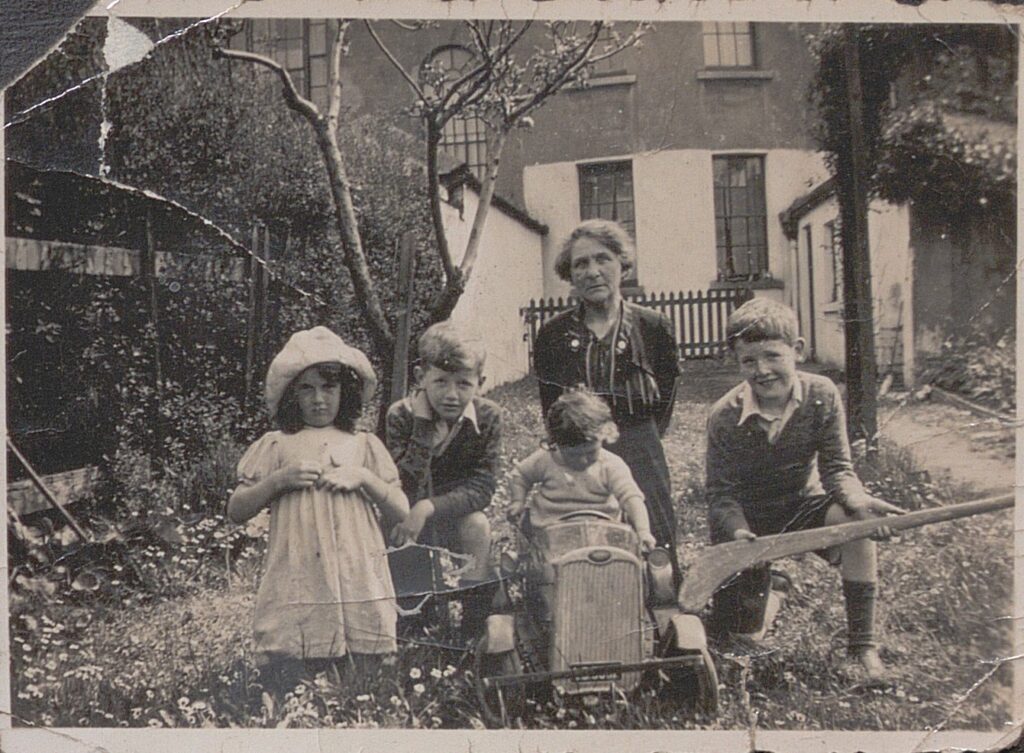 Black and white photograph depicting the Aunt of Kathleen Boland in the garden of the family home, with Kathleen's children.