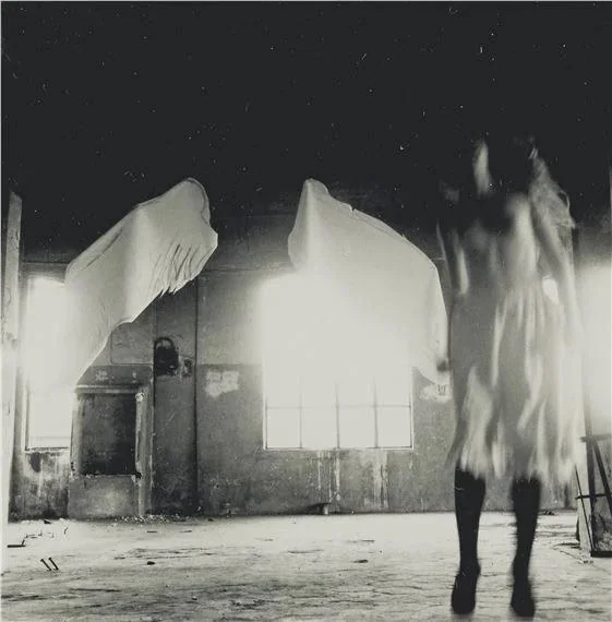 Black and white photography by Francesca Woodman of blurred figure in white skirt in foreground on the right. Self-portrait.