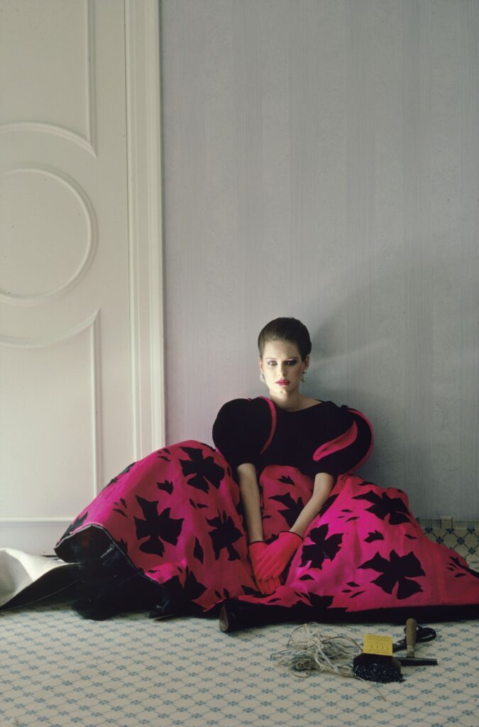 Colour fashion photograph by Alen MacWeeney. Woman sitting on floor wearing pink and black gown. Photographed for designer Arnold Scassi. This is an example of fashion photography.
