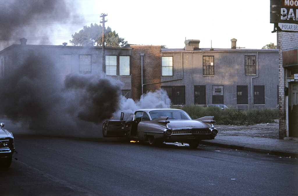 Car on fire, Detroit, Michigan. Colour photo by Alen MacWeeney. Black History Month.
