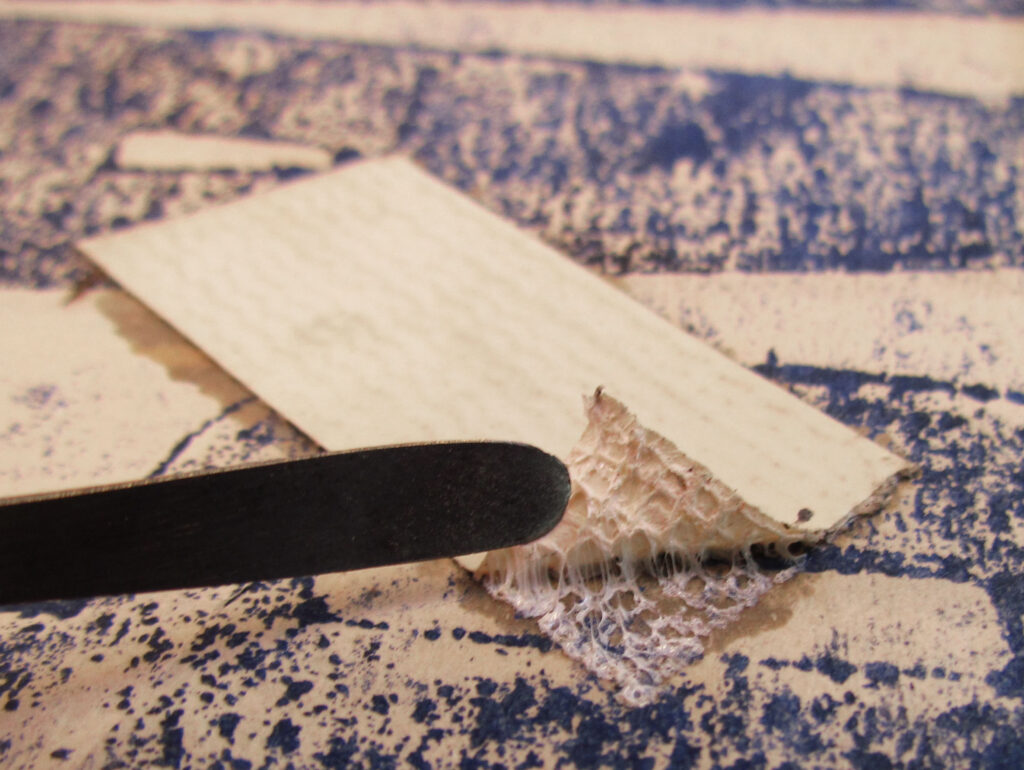 metal spatula lifts up tape stuck to paper to show sticky adhesive, it degrades and stains and damages the archive item paper underneath 