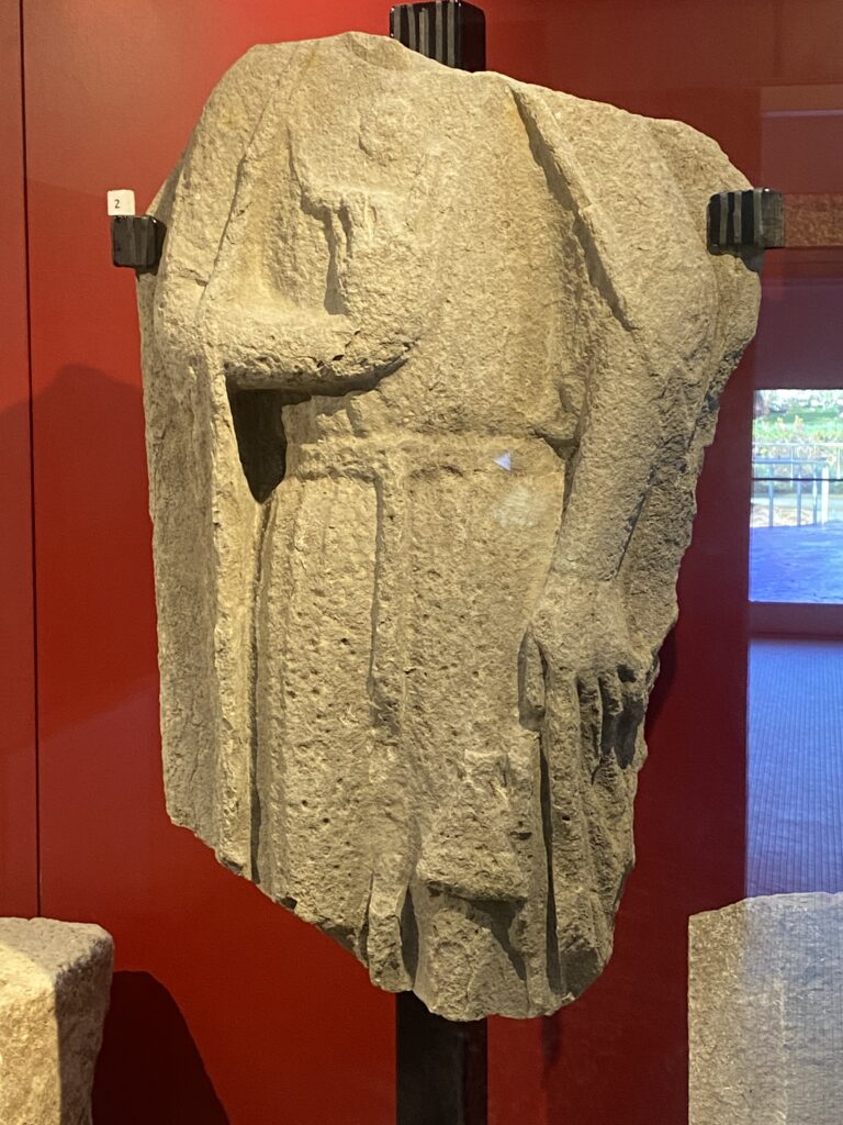 Photograph of an effigy in Cork Museum. The effigy has no head and no lower legs.