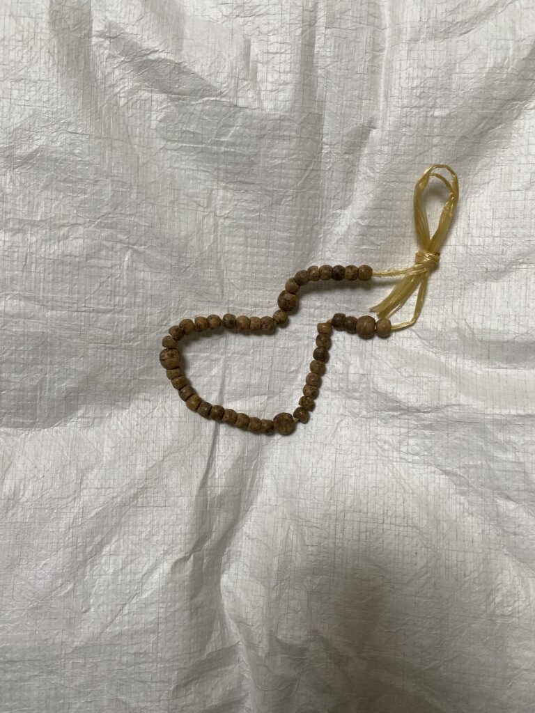 Photo of brown rosary beads tied with twine resting on a white cushion.