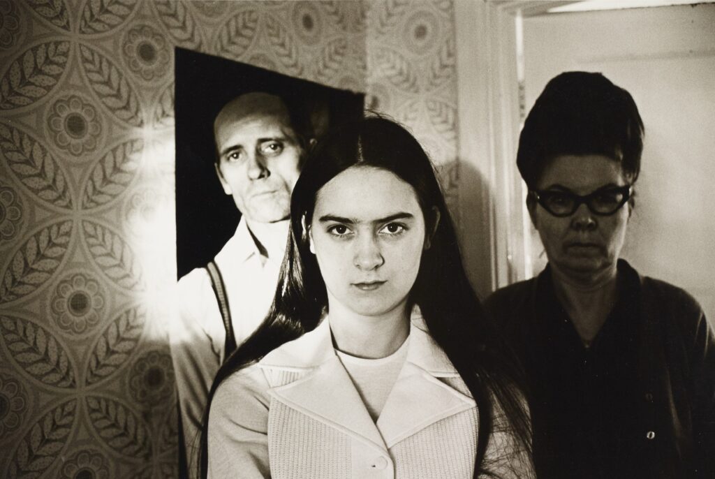 Younger female in foreground, older woman wearing glasses to the right behind, and male to the left behind woman in foreground.