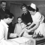 Nurses and doctors gathered around a child sitting on a exame table.