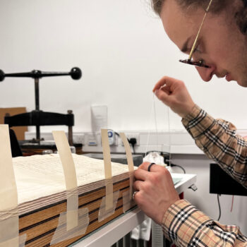 conservation intern pulls thread through the spine of the ledger, to sew it together.