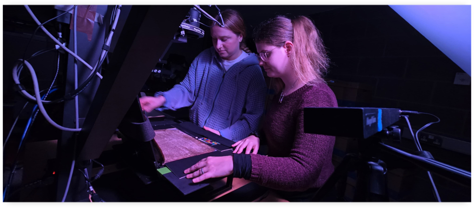 Two women examining a manuscript using the camera, pole and lights set up.