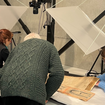 Three people examine a manuscript. Their backs are to the camera.
