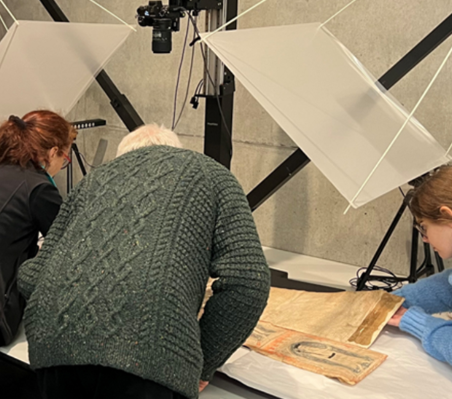 Three people examine a manuscript. Their backs are to the camera.